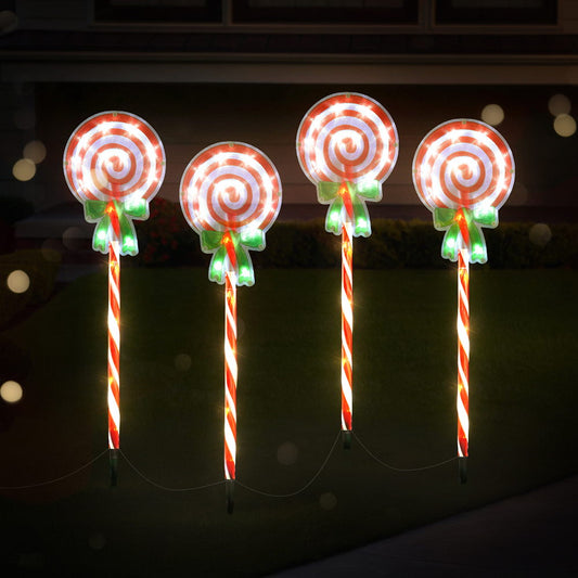 Four illuminated candy cane and lollipop decorations against a dark background.
