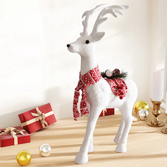 Decorative white reindeer with a red patterned scarf on a wooden surface with Christmas decorations.