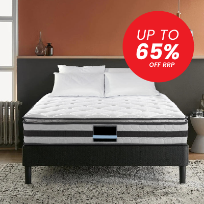 A white tufted mattress on a dark upholstered bed frame in a styled bedroom setting, with a large red promotional badge reading 'UP TO 65% OFF RRP' in the upper right.