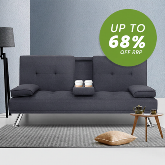 A dark gray fabric futon sofa with metal legs, shown in a styled room setting with a side table, lamp, and a green promotional circle overlay reading 'UP TO 68% OFF RRP'.