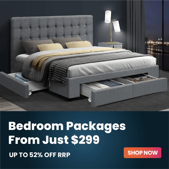A gray upholstered bed with a tall tufted headboard and matching storage footers, shown in a styled bedroom scene with bedding, pillows, lamps, and open storage drawers. A dark promotional banner at the bottom reads 'Bedroom Packages From Just $299 UP TO 52% OFF RRP' with a 'SHOP NOW' button.