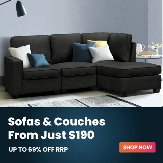 A dark charcoal gray sectional sofa with a chaise lounge on the right side, styled with white, blue, and yellow accent pillows. The sofa is set in a modern living room environment with a gray wall, a side table, and a rug.