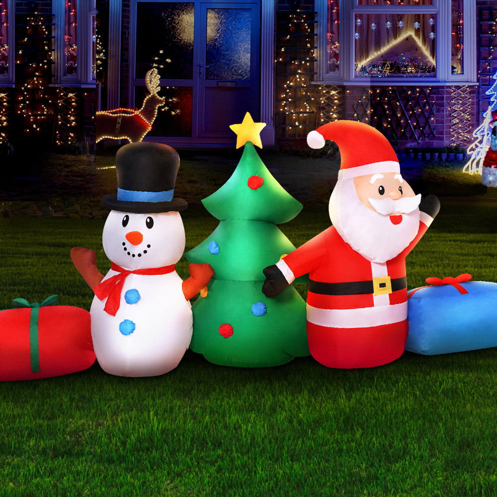Inflatable Christmas decorations including a snowman, tree, and Santa Claus on grass with a festive background.
