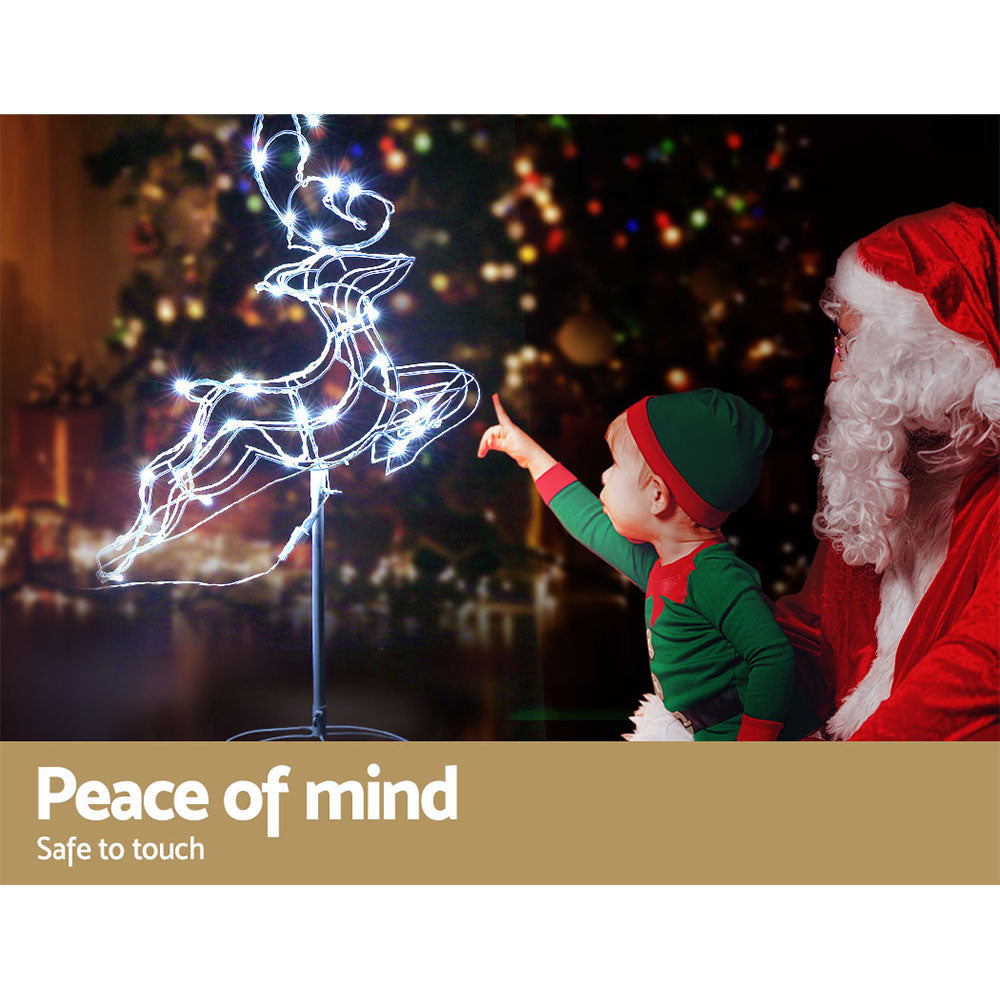 Santa Claus and a child with a lit reindeer decoration, Christmas tree in the background.